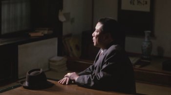 Movie still from “A City of Sadness” (1989), directed by Hsiao-Hsien Hou – A man sitting at a table in a dark room; Medium shot, Over the shoulder angle