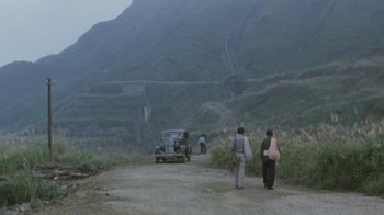 Movie still from “A City of Sadness” (1989), directed by Hsiao-Hsien Hou – Two people walking down a dirt road near a car; Extreme Wide shot, High angle