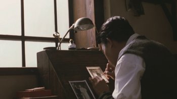 Movie still from “A City of Sadness” (1989), directed by Hsiao-Hsien Hou – A man sitting at a desk looking at a picture; Medium shot, High angle