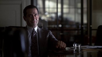 Movie still from “A Civil Action” (1998), directed by Steven Zaillian – A man in a suit sitting at a table with a drink; Close Up shot, Over the shoulder angle