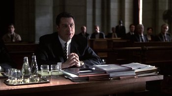 Movie still from “A Civil Action” (1998), directed by Steven Zaillian – A man sitting at a table in a courtroom; Medium shot, Low angle