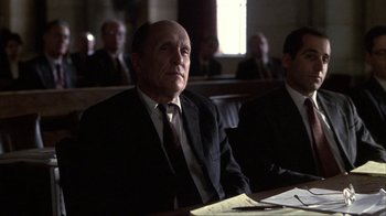 Movie still from “A Civil Action” (1998), directed by Steven Zaillian – An older man in a suit and tie sitting in a courtroom; Medium shot, Low angle