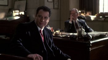 Movie still from “A Civil Action” (1998), directed by Steven Zaillian – A man sitting in a chair in front of a desk; Medium shot, Over the shoulder angle