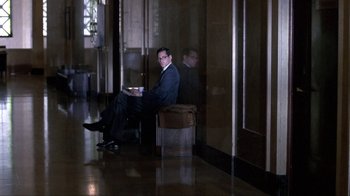 Movie still from “A Civil Action” (1998), directed by Steven Zaillian – A man in a suit sitting on a chair in front of a window; Wide shot, High angle