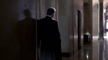 Movie still from “A Civil Action” (1998), directed by Steven Zaillian – A man in a black suit standing in a hallway; Wide shot, Over the shoulder angle