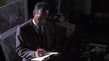 Movie still from “A Civil Action” (1998), directed by Steven Zaillian – A man in a suit writing on a piece of paper; Medium shot, High angle