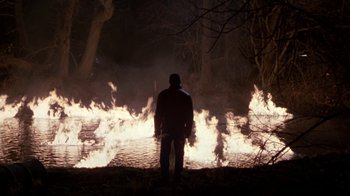 Movie still from “A Civil Action” (1998), directed by Steven Zaillian – A man standing in front of a fire in the woods; Wide shot, High angle