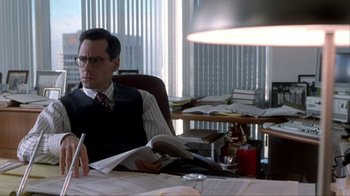 Movie still from “A Civil Action” (1998), directed by Steven Zaillian – A man sitting at a desk in a chair with a pen in his hand; Medium shot, Over the shoulder angle