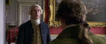 Movie still from “Tristram Shandy” (2005), directed by Michael Winterbottom – A man wearing a wig and a wig stand in front of a mirror; Medium shot, Over the shoulder angle