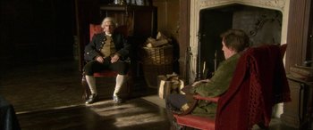 Movie still from “Tristram Shandy” (2005), directed by Michael Winterbottom – A man sitting in a chair in front of a fireplace; Wide shot, High angle