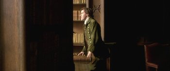 Movie still from “Tristram Shandy” (2005), directed by Michael Winterbottom – A man standing in front of a book shelf; Medium shot, Low angle