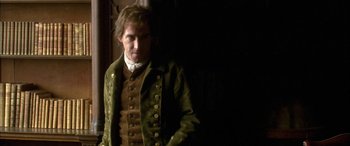 Movie still from “Tristram Shandy” (2005), directed by Michael Winterbottom – A man in a green jacket standing next to a wall; Medium shot, Over the shoulder angle