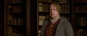 Movie still from “Tristram Shandy” (2005), directed by Michael Winterbottom – A man standing in front of a book shelf; Medium shot, Low angle