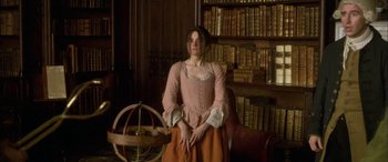 Movie still from “Tristram Shandy” (2005), directed by Michael Winterbottom – A woman sitting in front of a book shelf; Medium shot, High angle