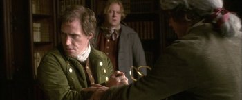 Movie still from “Tristram Shandy” (2005), directed by Michael Winterbottom – A man in a green jacket is holding a pair of scissors; Medium shot, Over the shoulder angle