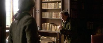 Movie still from “Tristram Shandy” (2005), directed by Michael Winterbottom – A man in a library with a book case in the background; Medium shot, Over the shoulder angle