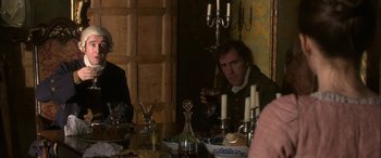 Movie still from “Tristram Shandy” (2005), directed by Michael Winterbottom – A man sitting in front of a table holding a wine glass; Medium shot, Over the shoulder angle