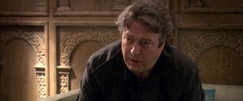 Movie still from “Tristram Shandy” (2005), directed by Michael Winterbottom – A person sitting on a couch near a fireplace; Close Up shot, Over the shoulder angle