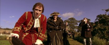 Movie still from “Tristram Shandy” (2005), directed by Michael Winterbottom – A group of people standing on top of a grass covered field; Medium shot, Over the shoulder angle