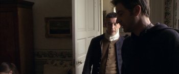 Movie still from “Tristram Shandy” (2005), directed by Michael Winterbottom – A man wearing a neck brace standing next to another man in front of a door; Medium shot, Over the shoulder angle