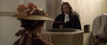 Movie still from “Tristram Shandy” (2005), directed by Michael Winterbottom – A man reading a book in front of a woman wearing a straw hat; Medium shot, High angle