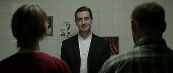 Movie still from “Department Q: A Conspiracy of Faith” (2016), directed by Hans Petter Moland – A man wearing a suit and tie standing in front of a wall; Medium shot, Over the shoulder angle