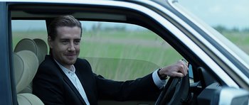 Movie still from “Department Q: A Conspiracy of Faith” (2016), directed by Hans Petter Moland – A man in a suit sitting in the drivers seat of a car; Medium shot, Over the shoulder angle