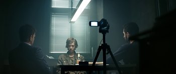 Movie still from “Department Q: A Conspiracy of Faith” (2016), directed by Hans Petter Moland – A man sitting at a table in front of a video camera; Medium shot, Over the shoulder angle