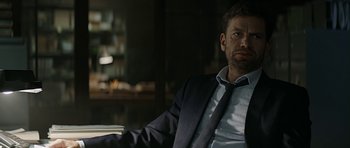 Movie still from “Department Q: A Conspiracy of Faith” (2016), directed by Hans Petter Moland – A man sitting in a chair wearing a suit and tie; Medium shot, Over the shoulder angle