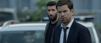 Movie still from “Department Q: A Conspiracy of Faith” (2016), directed by Hans Petter Moland – A man in a suit and tie standing next to another man in a suit and tie; Close Up shot, Over the shoulder angle