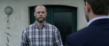 Movie still from “Department Q: A Conspiracy of Faith” (2016), directed by Hans Petter Moland – A man standing in front of another man in front of a building; Medium shot, Low angle