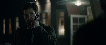 Movie still from “Department Q: A Conspiracy of Faith” (2016), directed by Hans Petter Moland – A man talking on a cell phone while standing outside of a building; Close Up shot, Over the shoulder angle