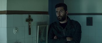 Movie still from “Department Q: A Conspiracy of Faith” (2016), directed by Hans Petter Moland – A man standing next to a cross in a room; Medium shot, Over the shoulder angle