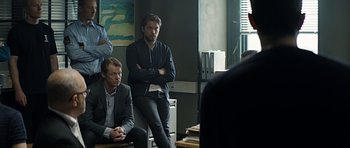 Movie still from “Department Q: A Conspiracy of Faith” (2016), directed by Hans Petter Moland – A group of men sitting next to each other in a room; Medium shot, Over the shoulder angle
