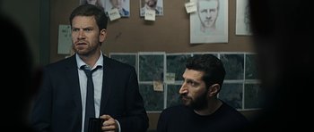 Movie still from “Department Q: A Conspiracy of Faith” (2016), directed by Hans Petter Moland – Two men in suits and ties are sitting in front of a wall; Medium shot, Over the shoulder angle