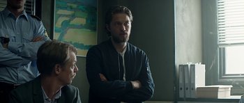 Movie still from “Department Q: A Conspiracy of Faith” (2016), directed by Hans Petter Moland – A man standing next to another man with his arms crossed; Medium shot, Over the shoulder angle