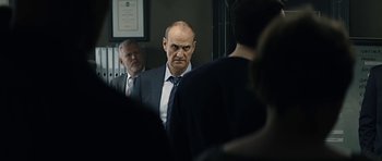 Movie still from “Department Q: A Conspiracy of Faith” (2016), directed by Hans Petter Moland – A man in a suit and tie standing in front of two other men; Medium shot, Over the shoulder angle