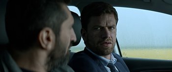 Movie still from “Department Q: A Conspiracy of Faith” (2016), directed by Hans Petter Moland – A man in a suit sitting in the back of a car; Close Up shot, Over the shoulder angle