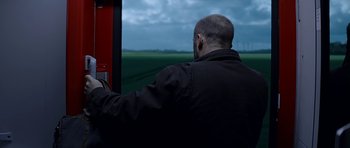 Movie still from “Department Q: A Conspiracy of Faith” (2016), directed by Hans Petter Moland – A man in a black jacket is looking out a window; Medium shot, Over the shoulder angle