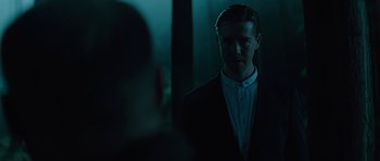 Movie still from “Department Q: A Conspiracy of Faith” (2016), directed by Hans Petter Moland – A man standing in a dark room looking at the camera; Medium shot, Over the shoulder angle