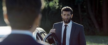 Movie still from “Department Q: A Conspiracy of Faith” (2016), directed by Hans Petter Moland – A man wearing a suit and tie holding a steering wheel; Close Up shot, Over the shoulder angle