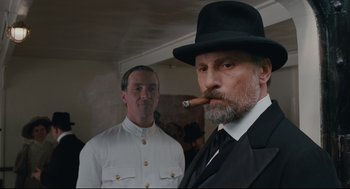 Movie still from “A Dangerous Method” (2011), directed by David Cronenberg – A man in a hat and a suit smoking a cigar; Medium shot, Low angle
