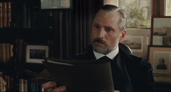 Movie still from “A Dangerous Method” (2011), directed by David Cronenberg – An older man sitting at a table looking at a piece of paper; Close Up shot, Low angle