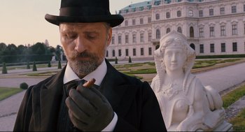 Movie still from “A Dangerous Method” (2011), directed by David Cronenberg – A man in a black suit and a black hat smoking a cigarette; Medium shot, Low angle