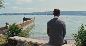 Movie still from “A Dangerous Method” (2011), directed by David Cronenberg – A man sitting on the edge of a pier looking out at the water; Wide shot, Over the shoulder angle