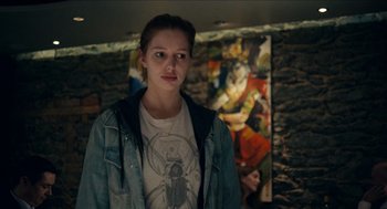 Movie still from “A Date for Mad Mary” (2016), directed by Darren Thornton – A woman standing in front of a painting in a room; Medium shot, Over the shoulder angle