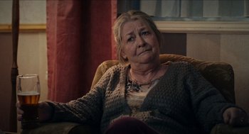 Movie still from “A Date for Mad Mary” (2016), directed by Darren Thornton – An older woman sitting in a chair looking at the camera; Close Up shot, Over the shoulder angle
