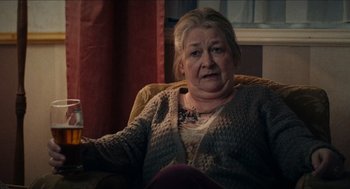 Movie still from “A Date for Mad Mary” (2016), directed by Darren Thornton – An older woman sitting in a chair in front of a window; Medium shot, Over the shoulder angle