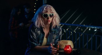 Movie still from “A Date for Mad Mary” (2016), directed by Darren Thornton – A woman sitting at a table holding a drink; Medium shot, Over the shoulder angle