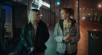 Movie still from “A Date for Mad Mary” (2016), directed by Darren Thornton – Two young women standing next to each other on the sidewalk; Medium shot, Over the shoulder angle